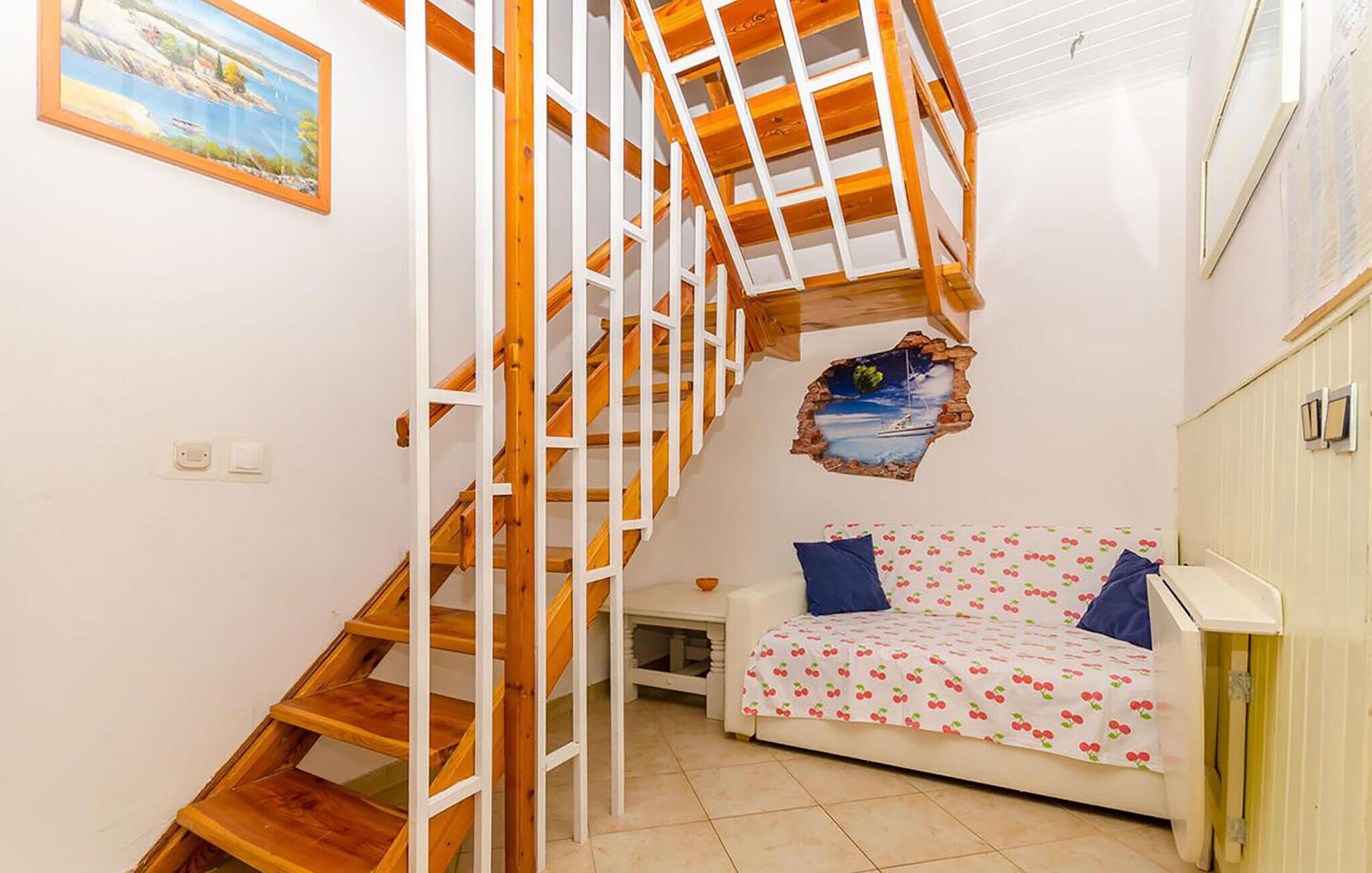 A bedroom with a wooden staircase, a bed with a cherry pattern, and a painting of a seascape.