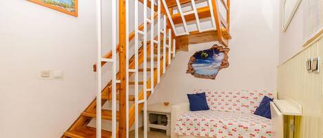 A bedroom with a wooden staircase, a bed with a cherry pattern, and a painting of a seascape.