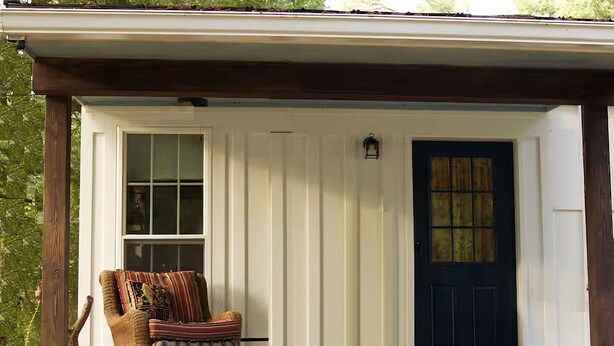 A small, single-story building with a porch, a dark blue door, and a wicker chair. - Charming 1-bedroom "glamping" cottage in peaceful Chapin [see description below] (Chapin)