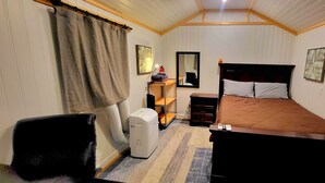 A bedroom with a bed, a desk, a chair, a heater, and a TV. - Charming 1-bedroom "glamping" cottage in peaceful Chapin [see description below] (Chapin)