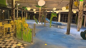An indoor play area with artificial plants, tables, chairs, and a slide. - LuxeHaven - A  Luxury Hot Tub Holiday Home at Tattershall Lakes Country Park (Tattershall)