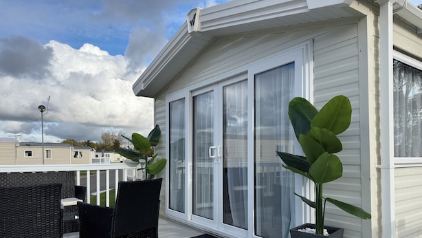 A covered outdoor area with a patio table and chairs, large sliding glass doors, and potted plants. - LuxeHaven - A  Luxury Hot Tub Holiday Home at Tattershall Lakes Country Park (Tattershall)