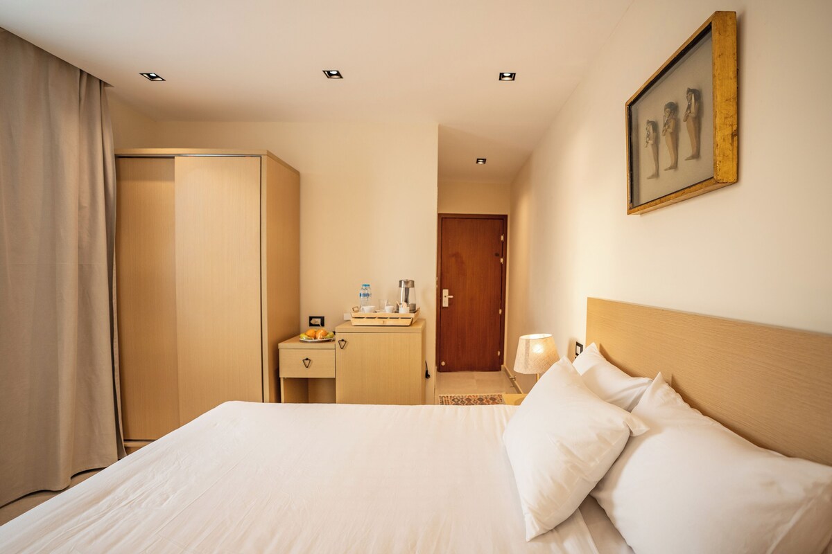 A hotel room with a bed, a nightstand, a desk, a wardrobe, and a framed picture on the wall.
