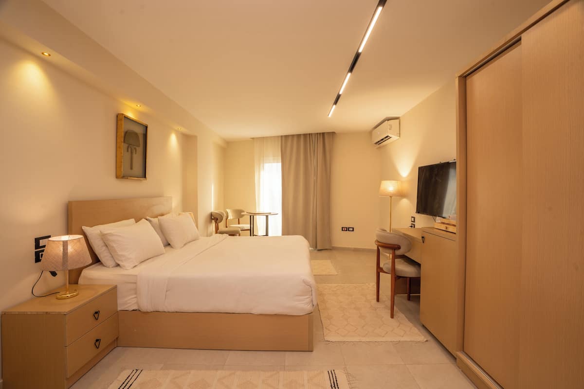 A modern hotel room with a large bed, bedside table, lamp, TV, and a wardrobe.