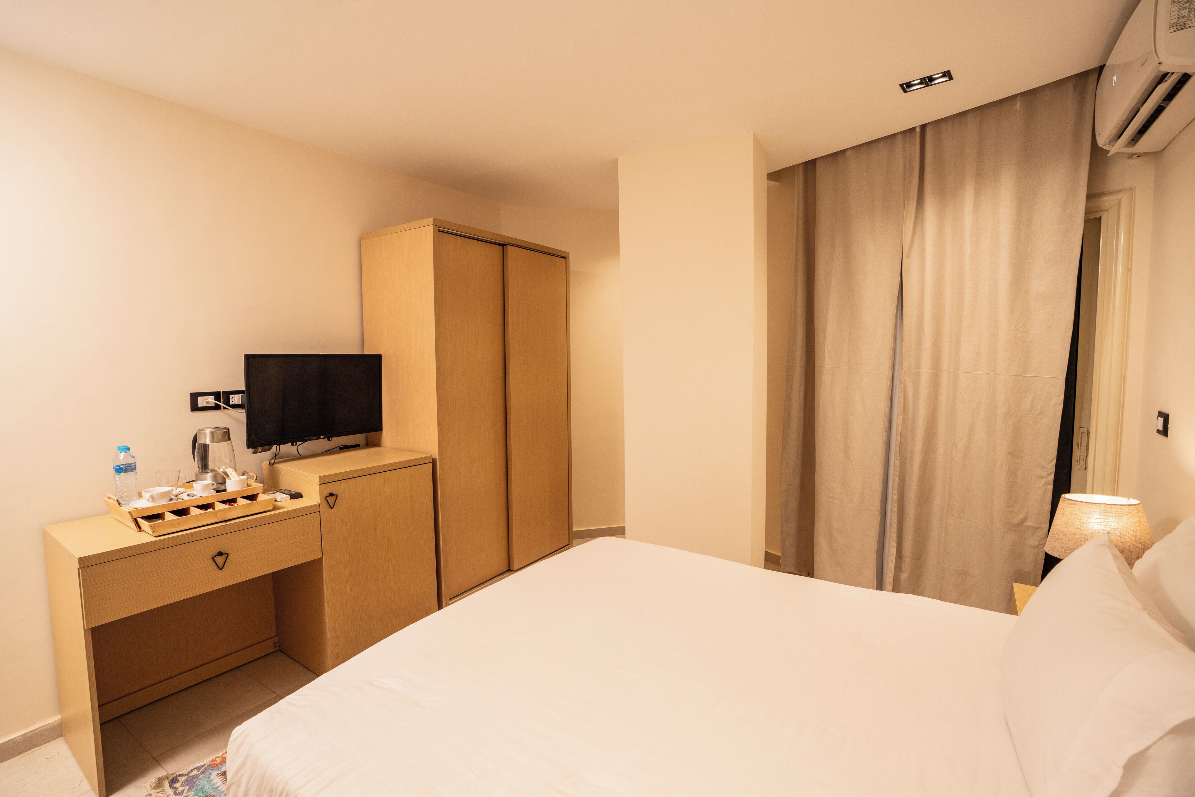 A hotel room with a bed, a desk with a television, a wardrobe, and a curtain.