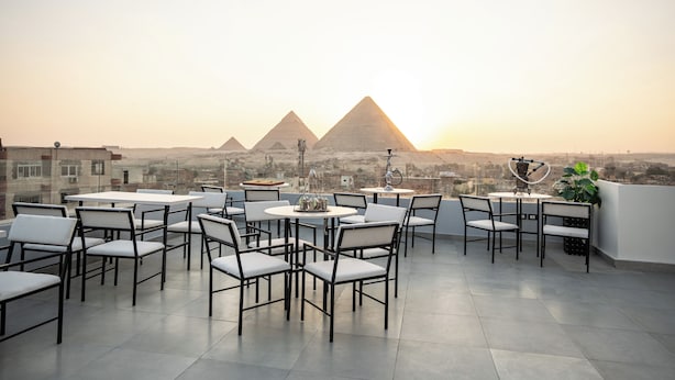 A rooftop terrace with tables and chairs, offering a view of the pyramids in the distance. - RIWAQ Pyramids Boutique  (Giza)