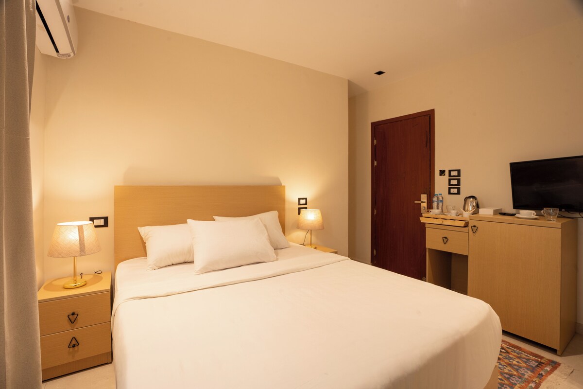 A hotel room with a bed, bedside lamps, a wooden nightstand, a wardrobe, and a television.