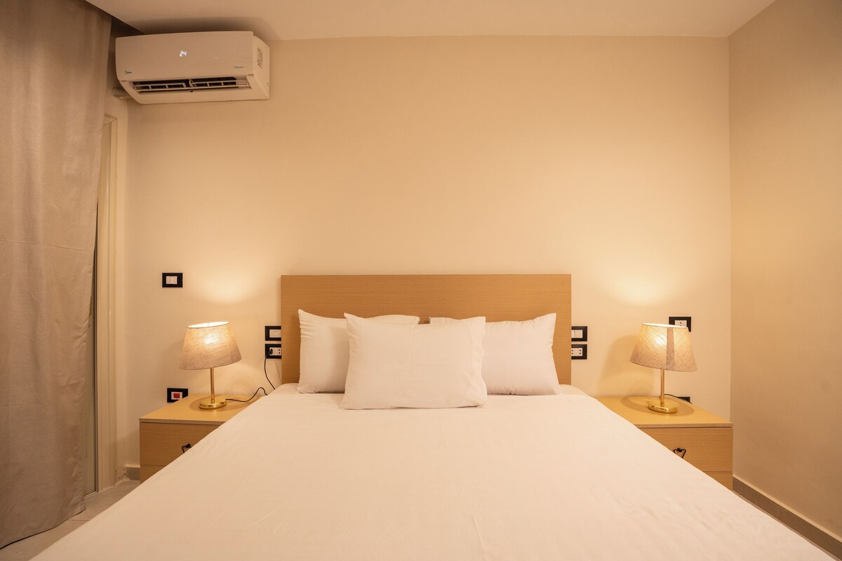 A neatly made bed with white linens and two bedside lamps.