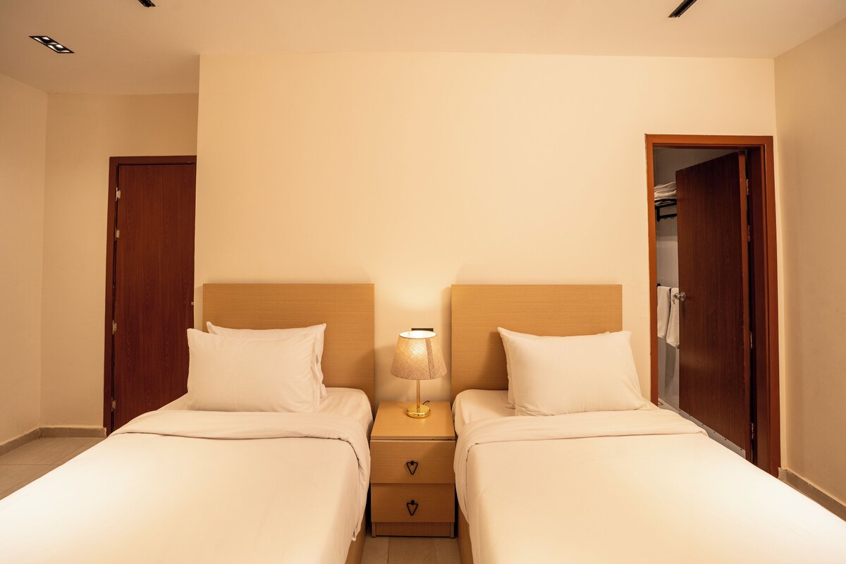A hotel room with two single beds, a nightstand with a lamp, and a wardrobe.