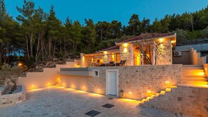 Una casa moderna con fachada de piedra, un espacio de estar al aire libre cubierto y una escalera que conduce a un segundo nivel.