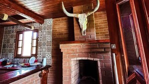 A rustic interior with a brick fireplace, wooden ceiling beams, and a large bull skull mounted above it. - La Domita (Camanducaia)