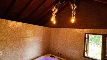 A spa room with a hot tub, wooden ceiling beams, patterned walls, and a window.