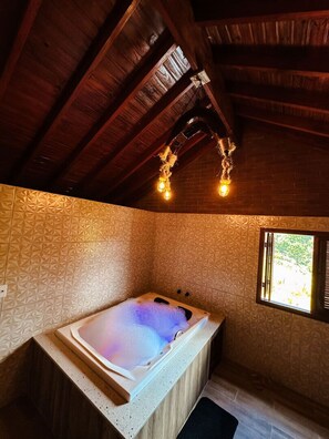 A spa room with a hot tub, wooden ceiling beams, patterned walls, and a window. - La Domita (Camanducaia)
