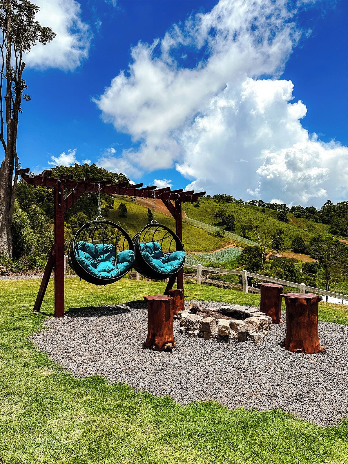 Un columpio con dos asientos, un pérgola de madera y un área de grava con una valla de madera al fondo.