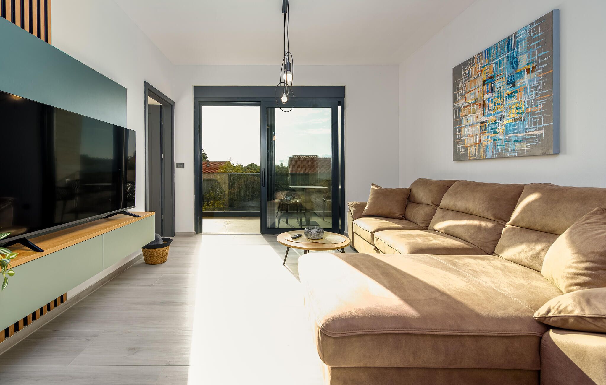 Un soggiorno moderno con un'ampia televisione a schermo piatto, un divano beige e una porta vetrata che dà su un patio esterno.
