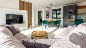A modern living room with a flat-screen TV, a sofa, a coffee table, and a dining area with chairs. - Beautiful home in Vir (Vir)