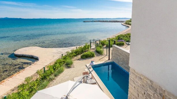 A pool with a clear view of the sea and a sandy beach area with steps leading to the pool. - Cozy home in Privlaka (Privlaka)