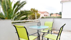 Eine kleine Terrasse im Freien mit einem runden Tisch, vier Stühlen, einer dekorativen Glasvase und einer Palme.