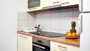Keittiössä on valkoiset kaapit, mikroaaltouuni, liesi ja hedelmäkulho, jossa on ananas ja appelsiineja.