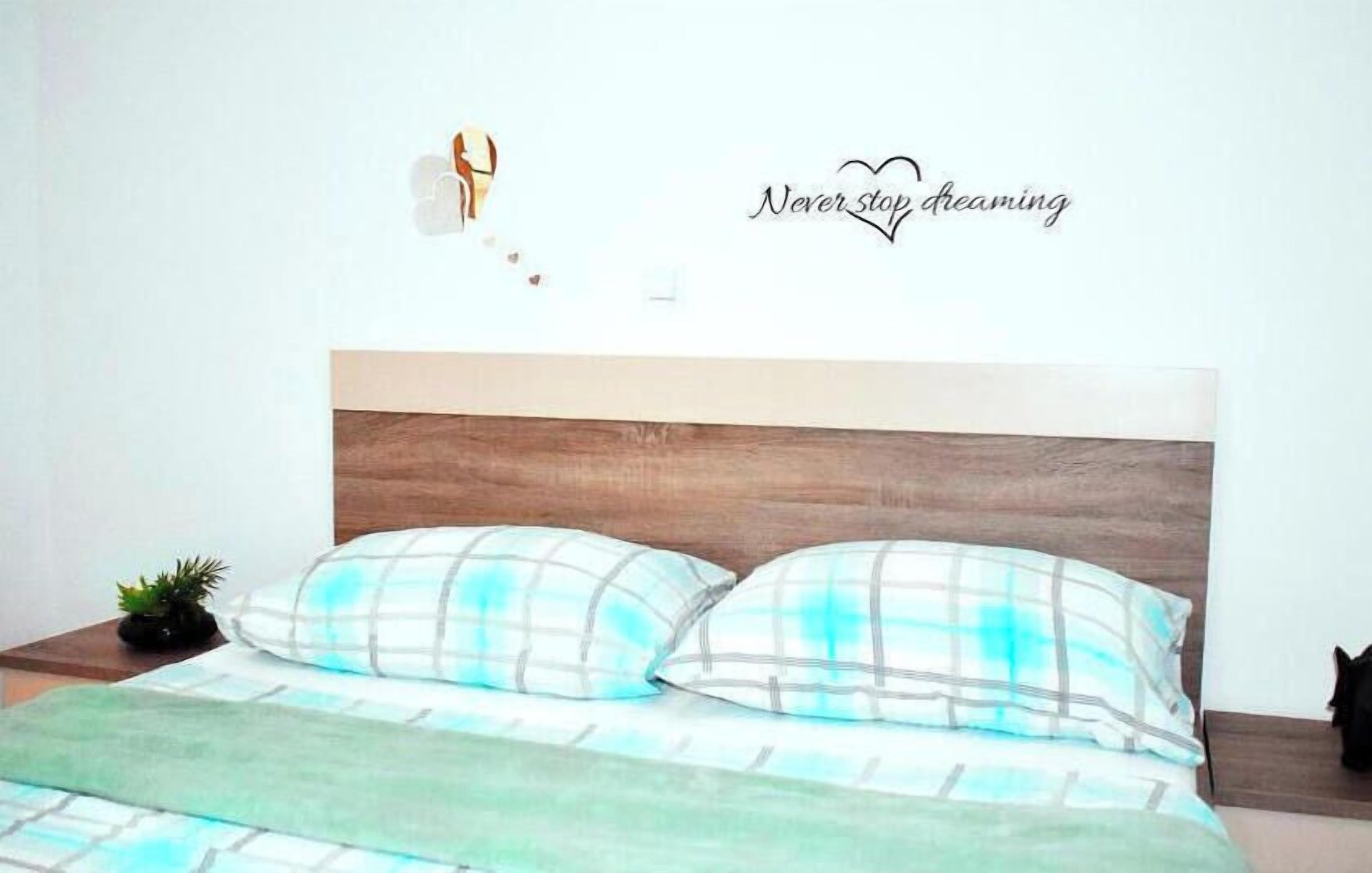A bed with a wooden headboard, two pillows, a green blanket, and a wall decoration with the text "Never stop dreaming".