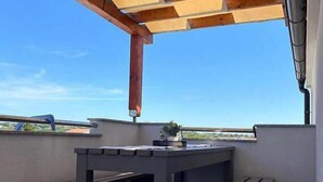 Eine Dachterrasse mit einer Holz-Pergola, einem Tisch mit Topfpflanze und freiem Blick auf die umliegende Landschaft.