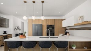 Cozinha moderna com uma ilha grande, banquetas, iluminação pendente e eletrodomésticos embutidos.