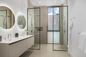 Ein modernes Badezimmer mit einer in Glas abgeschirmten Dusche, einem Doppelwaschtisch und einem großen Spiegel mit integrierter Beleuchtung.