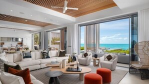 Un salon moderne comprenant un grand canapé, des fauteuils et des poufs, un coin repas et une cuisine.