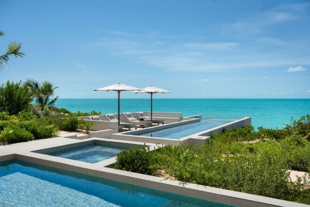 Une piscine à débordement moderne, dotée de chaises longues et de parasols, offrant une vue imprenable sur un océan d’un bleu profond.