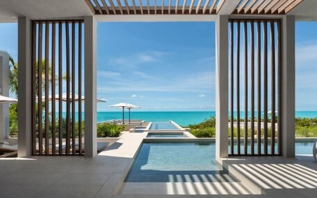 A modern resort with a pool leading to the beach, framed by vertical blinds.