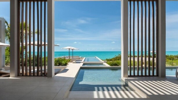 Un complexe hôtelier moderne doté d’une piscine qui donne directement sur la plage, le tout agrémenté de stores verticaux.