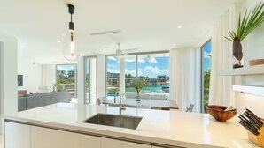 Une cuisine moderne dotée d’un grand îlot central, d’un évier intégré et offrant une vue sur une piscine et un jardin.