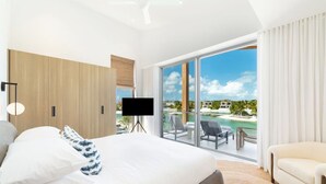 A modern hotel room with a large bed, a flat-screen TV, and a balcony with a view of a pool and resort. - Long Bay Dream | Modern Seaside Villa w/ Private Pool & Lounge | Relaxing Spa (Long Bay Hills)