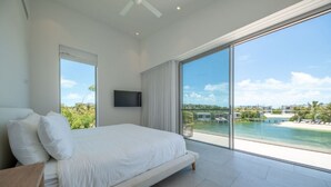 A bedroom with a large bed, a TV, and a view of a beach and ocean. - Turks Adventure | Kayak, Snorkel & Explore Turks’ Ocean Lagoon | Private Pool (Long Bay Hills)