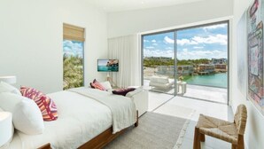 Quarto moderno com uma cama grande, televisão e varanda com vista para uma marina.