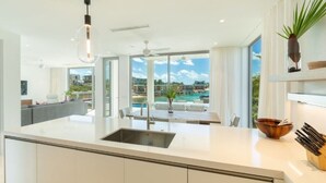 Een moderne keuken met een groot kookeiland, uitzicht op een zwembad en een eethoek met terrasoverdekking.