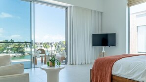 Ein modernes Hotelzimmer mit einem großen Bett, einem Flachbildfernseher, einem Balkon mit Meerblick und einem kleinen Tisch mit einer Pflanze.