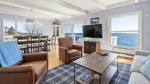 A spacious living area with a large window overlooking the sea, a television, and a dining area with a view.