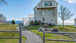 A two-story house with a balcony, a gravel pathway, and a view of the water.