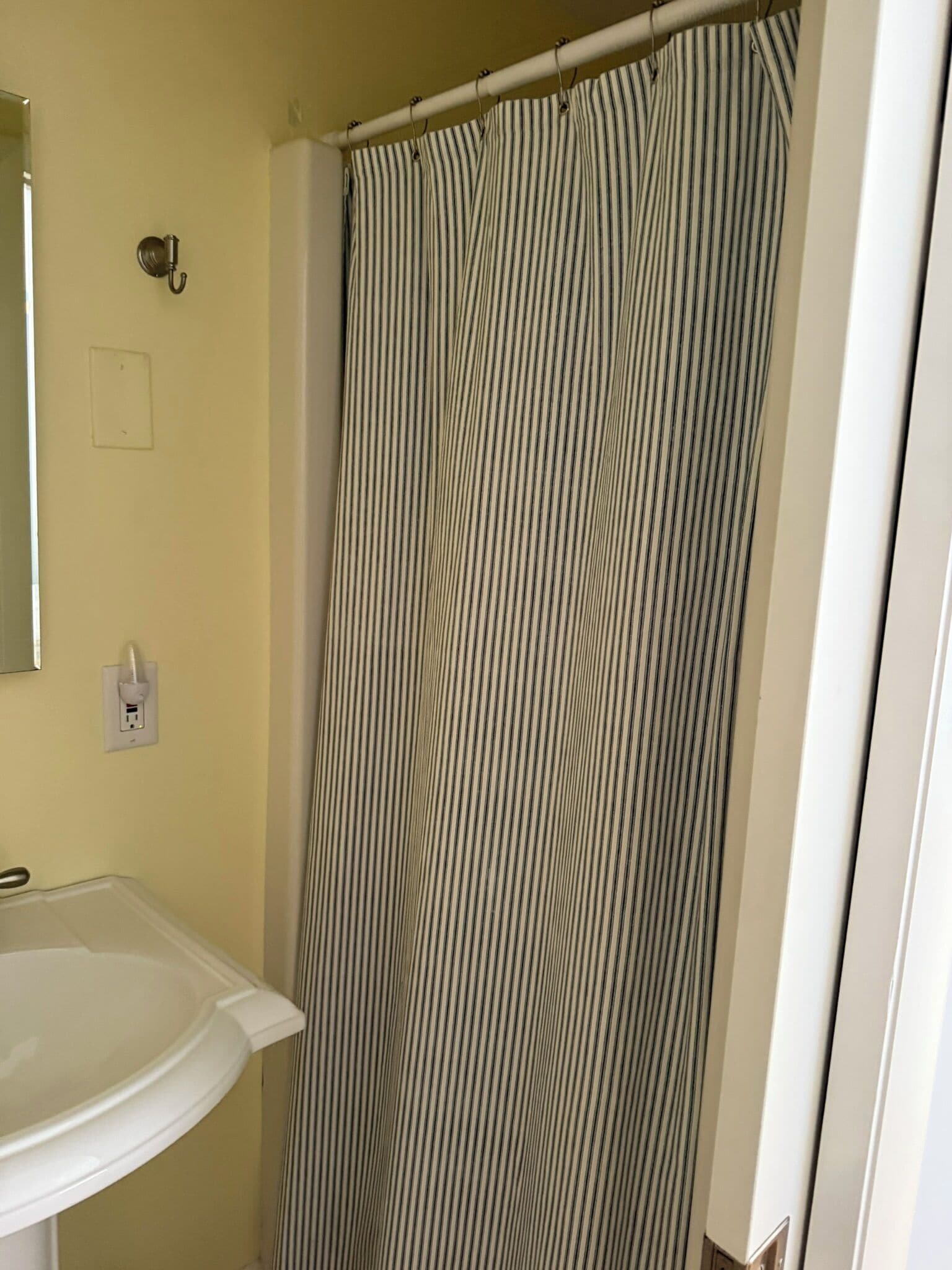 Een badkamer met een gordijn met strepen, een witte wastafel en een spiegel.