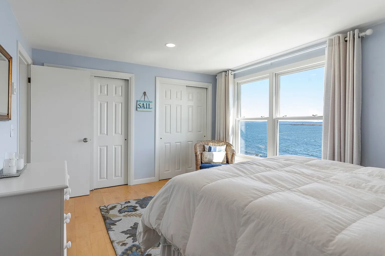 A bedroom with a large bed, a view of the sea, and a sign on the door that reads "Sail".