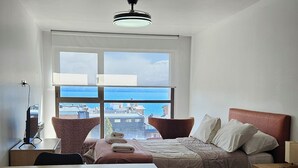A modern hotel room with a large window offering a city view, a bed with a red headboard, a desk with a chair, and a ceiling fan. - Comfortable and central studio with view to Nahuel Huapi lake (San Carlos de Bariloche)