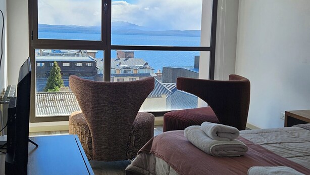 A modern hotel room with a large window offering a view of the city and sea. - Comfortable and central studio with view to Nahuel Huapi lake (San Carlos de Bariloche)