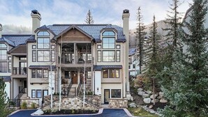 A multi-story residential building with a central staircase, stone landscaping, and surrounding evergreen trees. - Ski Chalet Beaver Creek - Ski In/Ski Out, Hot Tub (Beaver Creek)