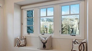A room with a large window, a bench with decorative pillows, and a view of trees and buildings. - Ski Chalet Beaver Creek - Ski In/Ski Out, Hot Tub (Beaver Creek)