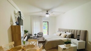 Ein modernes, helles Zimmer mit einem Bett, einer Couch, einem Esstisch mit Stühlen und einem Deckenventilator.