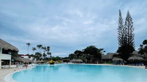 Ein Pool mit blauen Liegestühlen und ein strohgedecktes Gebäude im Hintergrund.