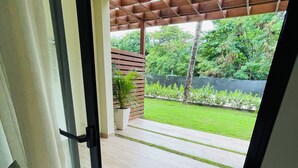 Eine Holzterrasse mit einer Pergola, einem Blumentopf und Blick auf einen gepflegten Rasen und Bäume.