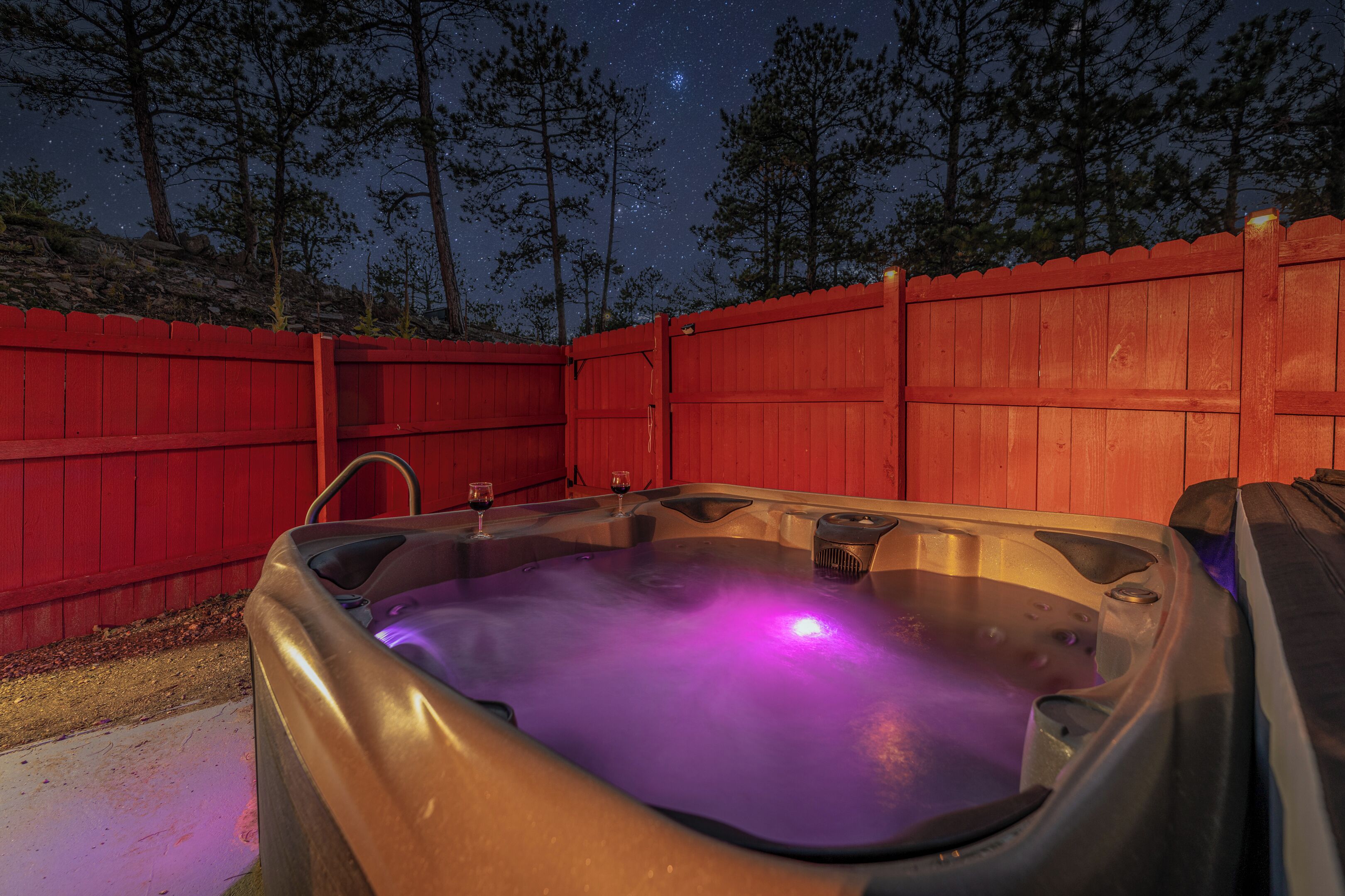 A hot tub with a wooden fence and trees in the background.