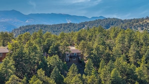 Una casa de dos pisos rodeada de un bosque denso, con una cadena montañosa al fondo.